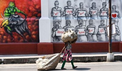 Girl in Calcutta, India walks with collected waste in front of a Corona awareness poster.